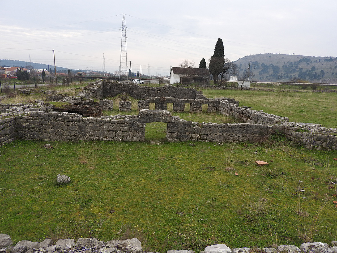 This photograph showcases part of the small Roman baths as seen from the decumanus, one of the main streets of the ancient city. The stone walls and internal structures, including some elements of the hypocaust heating system, are still well preserved. This thermal complex was likely an important space for social and hygienic life in Doclea.