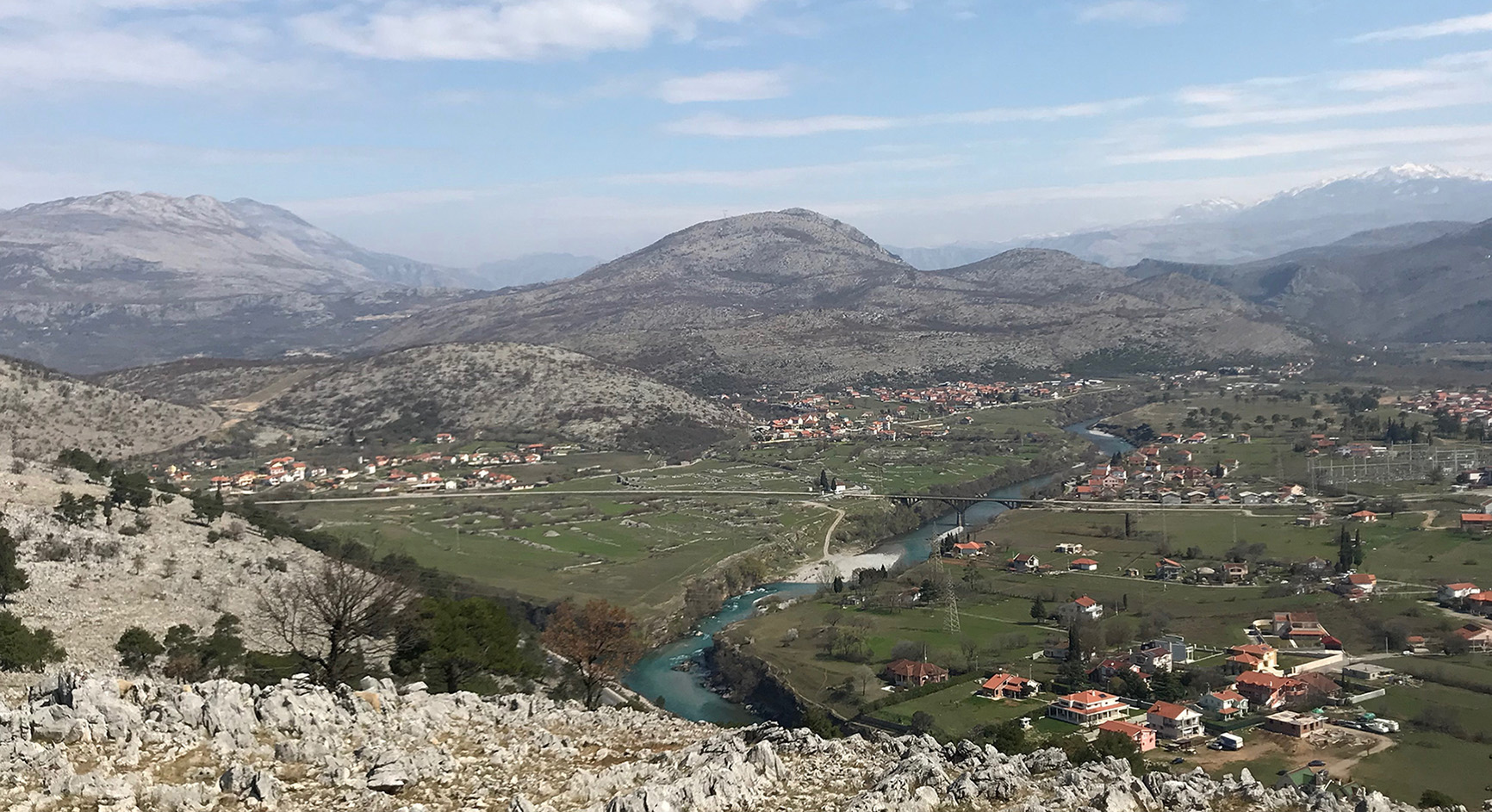 A panoramic view of the archaeological site of Doclea, with hills and mountains in the background. The hilly landscape surrounds the ancient ruins.